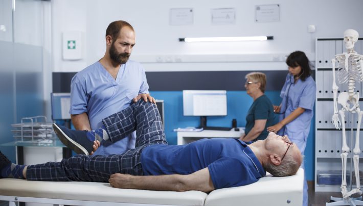 Healthcare specialist massaging legs muscles of senior patient, using alternative medicine to increase mobility in rehabilitation clinic. Male osteopath doing physical therapy for retired old man.